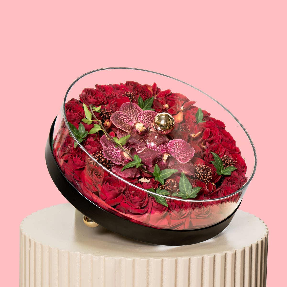 Decorative glass bowl filled with red flowers on a pink background