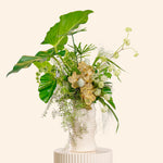 Floral arrangement with green leaves and white flowers in a white vase on a beige background