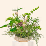 Decorative plant arrangement with greenery and white eggs on a beige pedestal against a light beige background