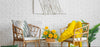 Rattan chairs with cushions and a small table with flowers against a white brick wall.