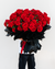 Person holding a large bouquet of red roses wrapped in black paper against a white background