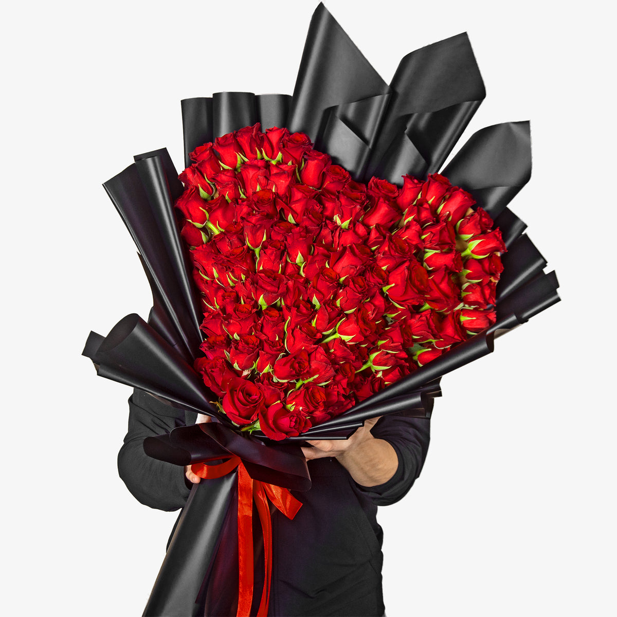 Bouquet of red roses wrapped in black paper with a red ribbon, held by a person.